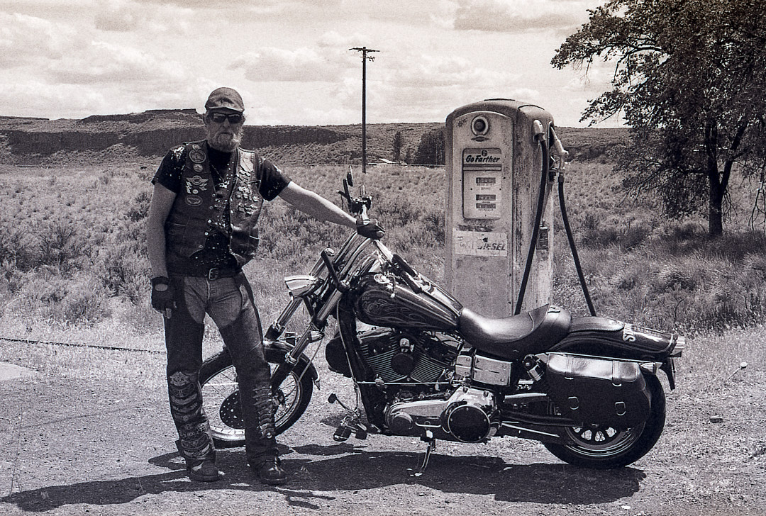Motorcyclist beside a vintage gas pump in open country