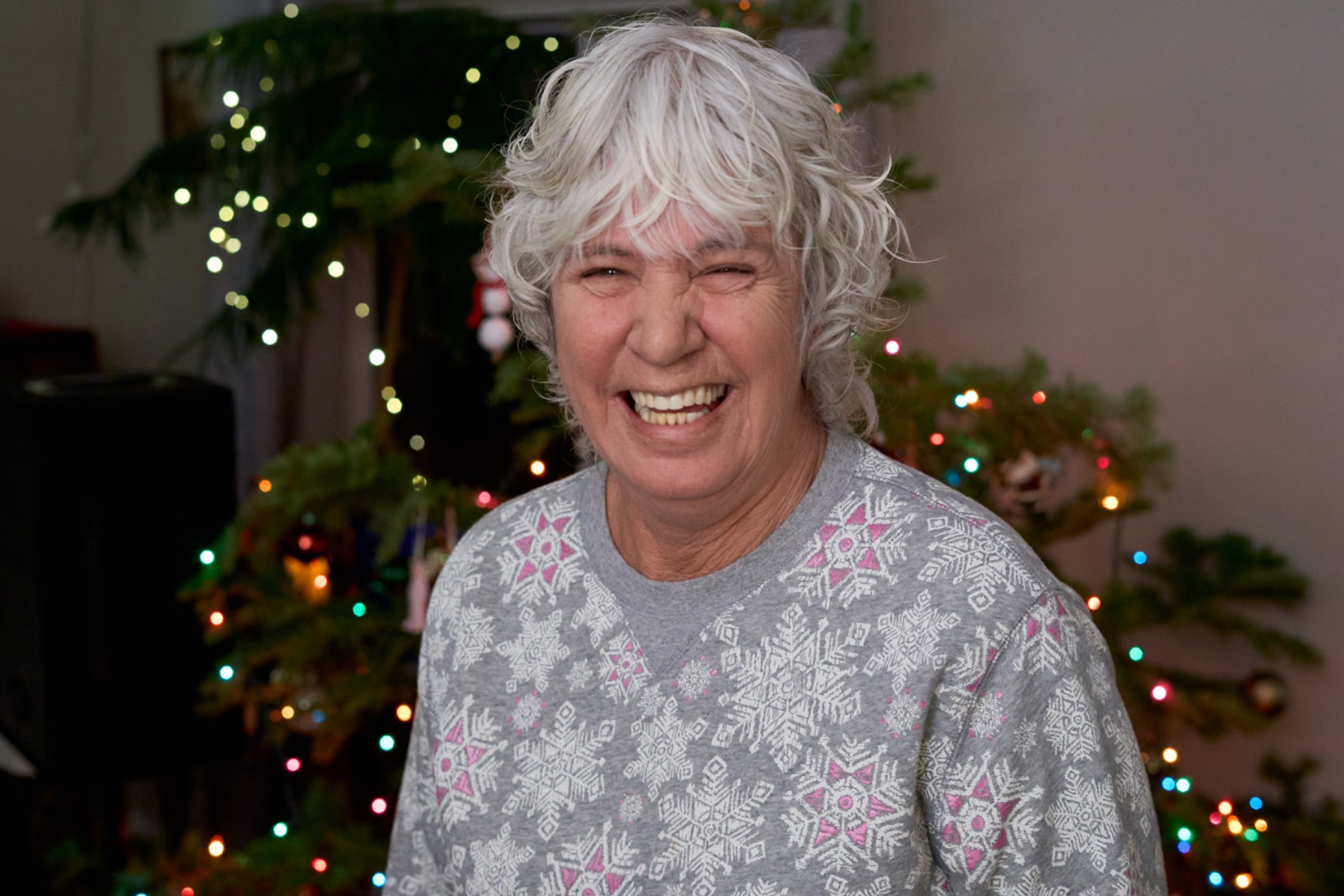 A silver haired woman laughing in front of Christmas lights